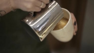 Barista holding a cup makes flavored cappuccino, pours milk into coffee