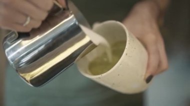 Handheld shot of matcha latte tea pouring with milk