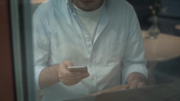 Tilt up shot of man with a phone typing in a laptop sitting indoors in a cafe — Stock Video