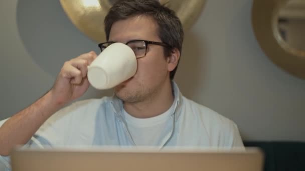 Primer plano del hombre en anteojos trabajando con un ordenador portátil bebiendo café — Vídeo de stock