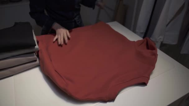 Handheld shot of woman folding a red sweatshirt on a table — Stock video