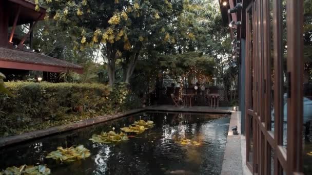 Снимок в реальном времени уютного двора ресторана с прудом, где плавают кои-карпы в Бангкоке, Таиланд. — стоковое видео