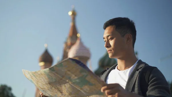 Portrét mladého Asiata, jak se dívá na mapu. Katedrála Vasilije Blahoslaveného na pozadí, Moskva Rusko. Oblast červeného náměstí. — Stock fotografie