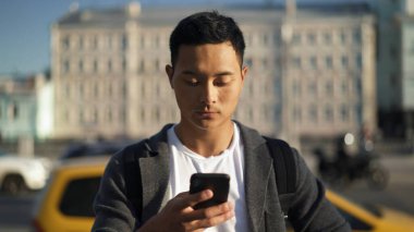 Portrait shot of a young Asian man looking at phone in Moscow. Tourist in Moscow. Freelance concept. clipart
