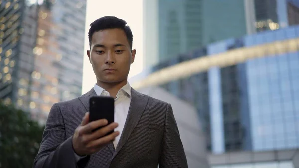 Vista frontale di un giovane uomo d'affari asiatico, leader corrispondenza al telefono. Quartiere centro città . — Foto Stock