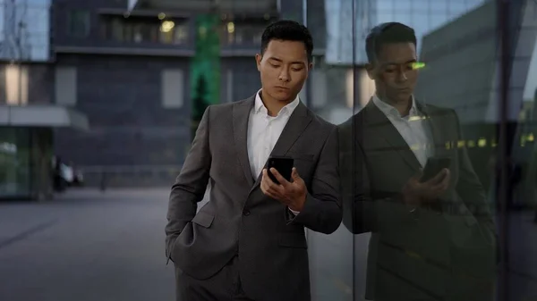 Přední pohled na mladého asijského obchodníka, který vede korespondenci po telefonu. Centrum města. — Stock fotografie