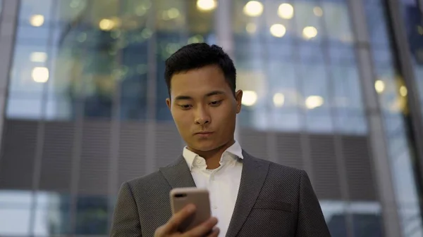 Vista frontale di un giovane uomo d'affari asiatico, leader corrispondenza al telefono. Quartiere centro città . — Foto Stock