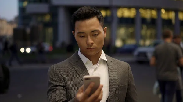 Front view of a young asian businessman, leading correspondence on the phone. Downtown district. Night time at business city.