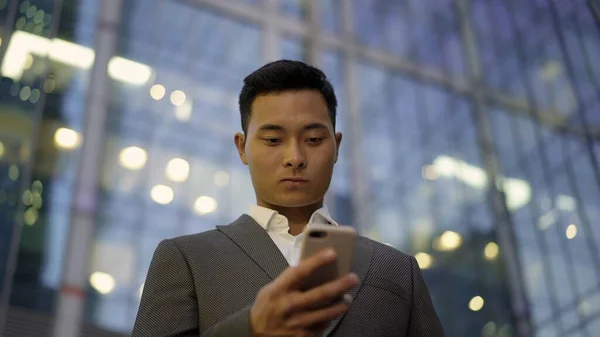 Laag zicht op een jonge Aziatische zakenman, leidende correspondentie aan de telefoon. Stadsdeel. — Stockfoto