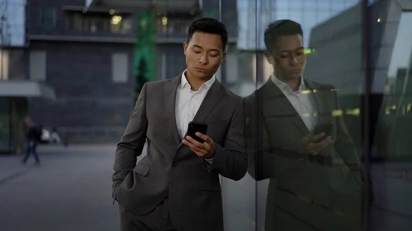 Vooraanzicht van een jonge Aziatische zakenman, leidende correspondentie aan de telefoon. Stadsdeel. — Stockfoto