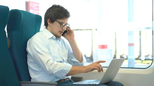 Young manager wearing a white shirt and jeans is riding a train to work and using his laptop. — Stock Photo, Image
