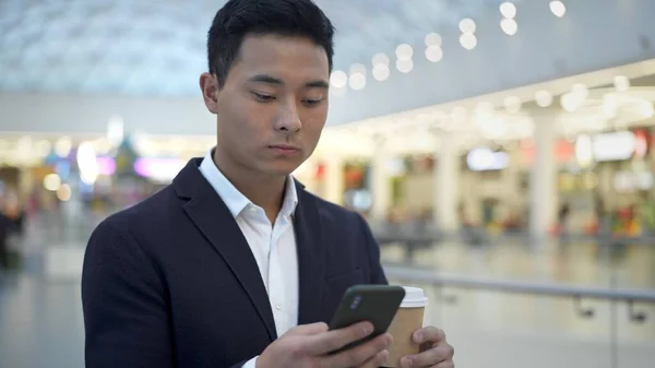Азіатський молодий бізнесмен в костюмі п'є текст кави по телефону. — стокове фото