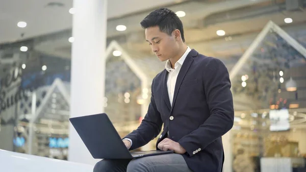 Вид збоку Середній знімок азіатського бізнесмена в костюмі, що працює з ноутбуком на колінах — стокове фото