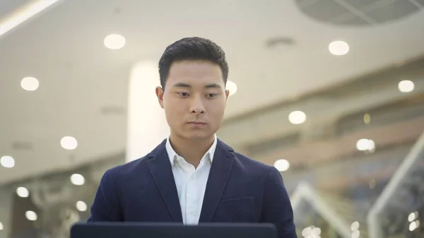 Framsidan av asiatisk man affärsman i kostym arbetar med laptop på knä — Stockfoto