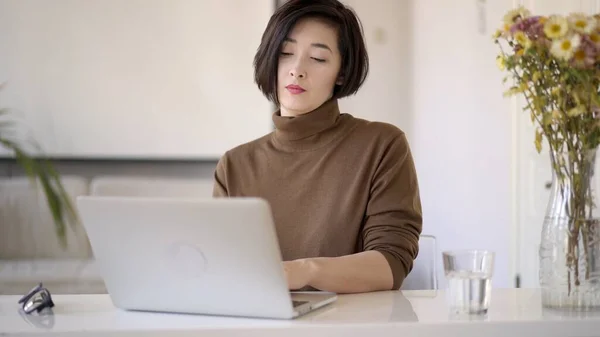 Gözlüklü Asyalı kadın, beyaz ev ofisinde dizüstü bilgisayarla çalışıyor. — Stok fotoğraf