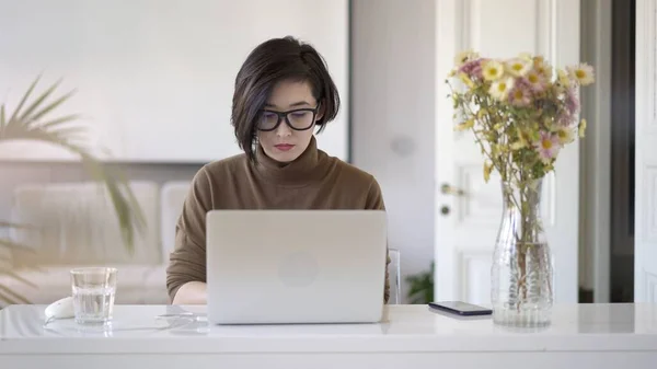 Asiática mujer en gafas de trabajo con portátil en blanco oficina en casa — Foto de Stock