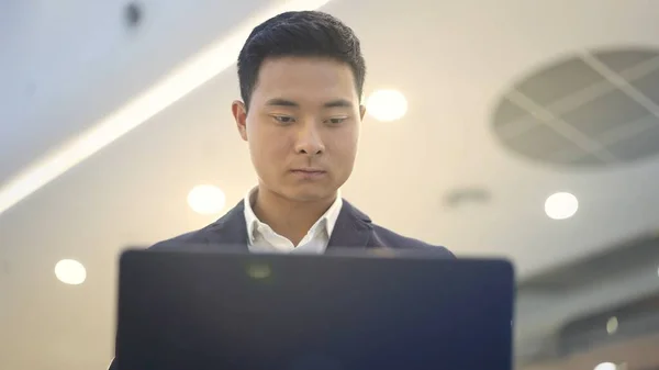 Framsidan av asiatisk man affärsman i kostym arbetar med laptop på knä — Stockfoto