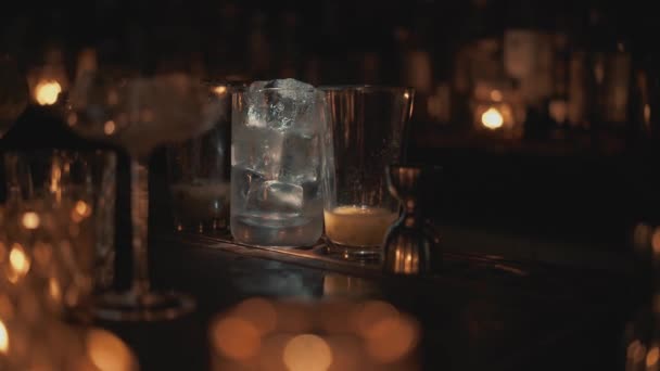 Colpo ravvicinato in tempo reale di un bicchiere con ghiaccio in piedi sul bancone. Un barista prepara cocktail in un bar a Bangkok . — Video Stock