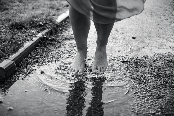 The girl is walking barefoot in a puddle.