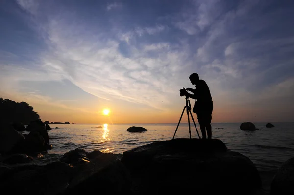 Silhouette a photographer taking pictures of sunrise on a rock, near the tropical beach