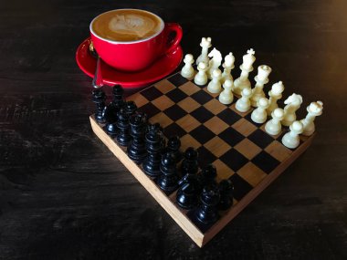 Kırmızı bir fincan sıcak cappuccino bir fincan satranç romantik bir ışık altındaki ahşap masa üstünde bir dizi. Lüks, eğitim ve yaşam tarzı kavramsal.