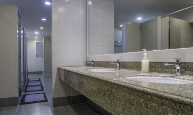 Erkekler tuvaletinde lavabolu musluklar granit tezgahın üzerinde.