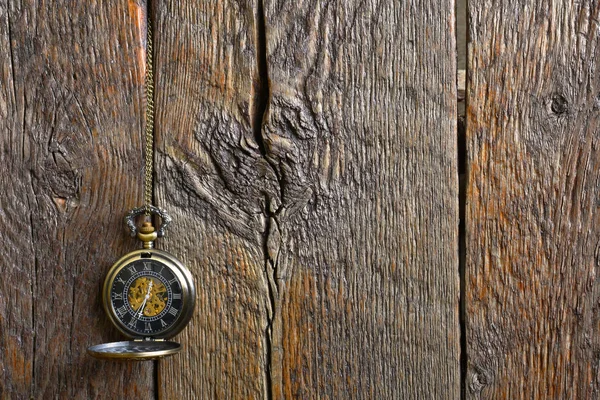 An image of an old antique pocket watch hanging against an old wooden background.