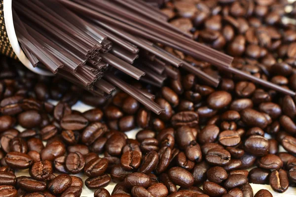 A low angle image of roasted coffee beans and brown plastic stir sticks.