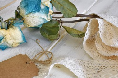 Krem renkli dantel ve kahverengi hediye etiketi ile eski bir soluk ve solmuş gül görüntüsünü yakından. 