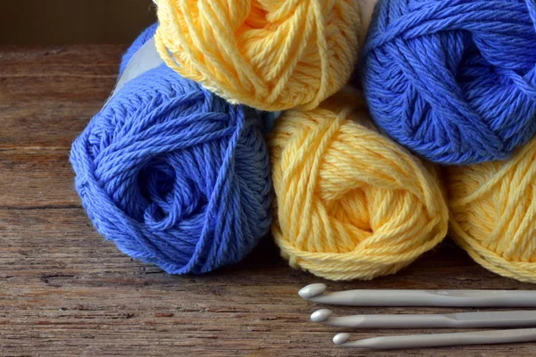 かぎ針編みの糸と木製のテーブルの つのかぎ針編みフックの青と黄色のボールのイメージに近い — ストック写真