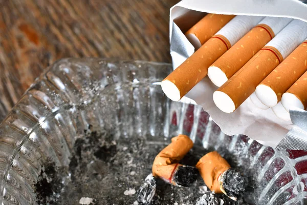 A close up image of an open package of cigarettes with a dirty used ashtray.