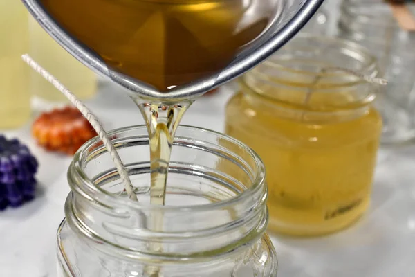 A close up image of pouring melted candle wax into glass molds for a small home-based candle making business.