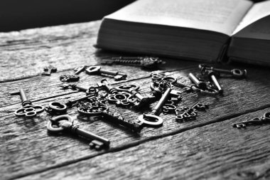 Bir siyah beyaz görüntü antika anahtarları ve ahşap bir masa üzerinde açık bir kitap.