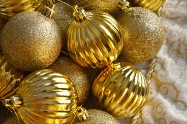 Beyaz kumaş arka planda parıldayan altın Noel ağacı süslemelerinin en üst görüntüsü.