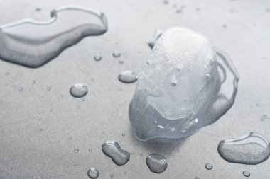 Gri metal bir plaka üzerinde eriyen tek bir buz küpünün yakın plan görüntüsü..