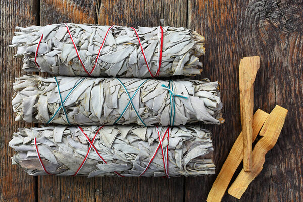 A close up image of three white sage smudge sticks and palo santo sticks used in energy clearing and healing.
