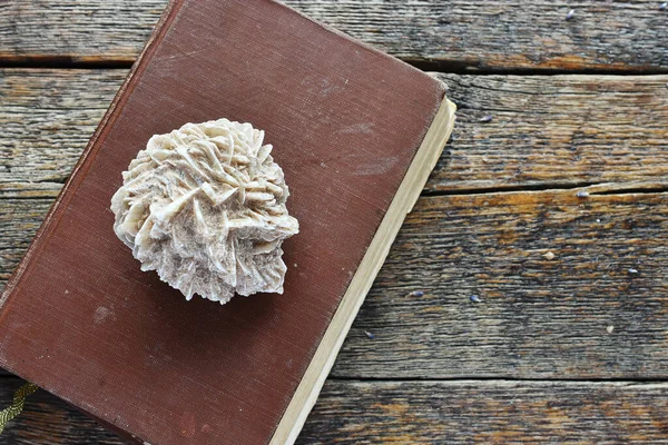 A top view image of a desert rose crystal and old vintage book and a wooden table top.