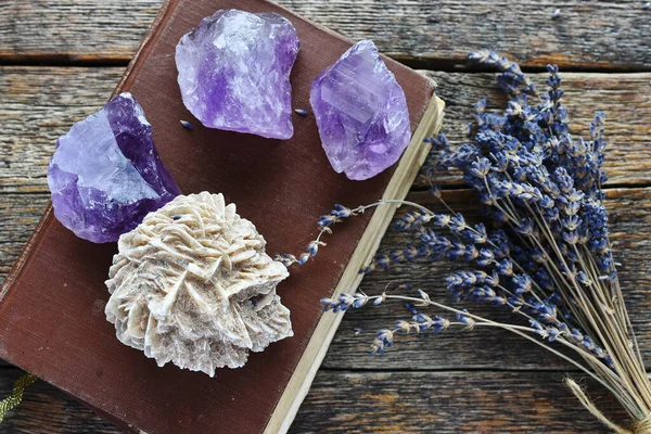 A top view image of amethyst and desert rose crystals on an old brown book with dried lavender flowers.