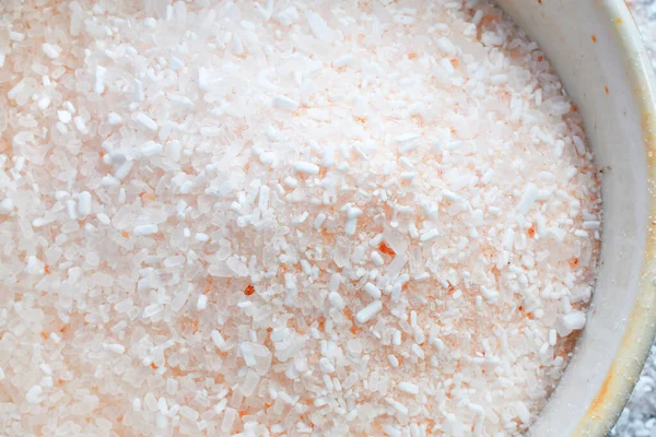 A close up image of pink Himalayan salt crystals in a light colored handmade pottery bowl.