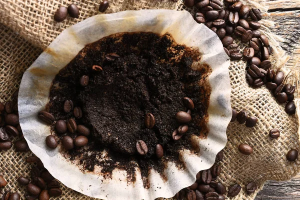 An image of a used coffee filter with coffee beans and burlap cloth on an old wooden table.