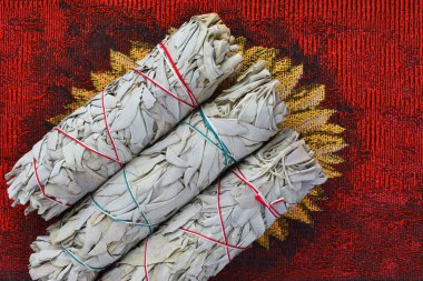 A top view image of three white sage bundles on a bright red fabric background.  clipart