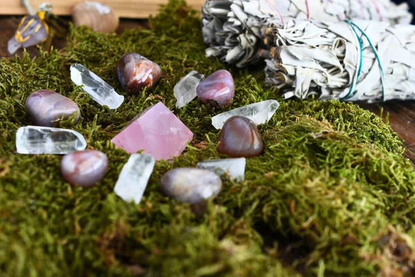 A close up image of a crystal energy healing grid on moss with various smudge sticks.