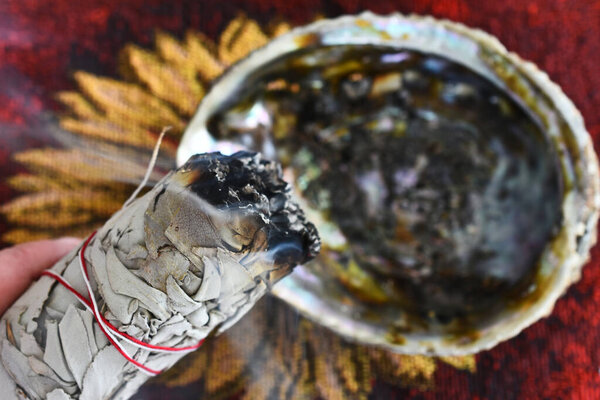 A close up image of a hand holding a burning white sage smudge stick. 