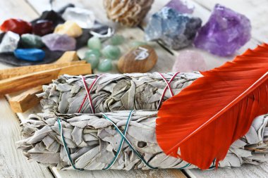 A close up image of two white sage bundles with orange sacred feather and healing crystals.  clipart