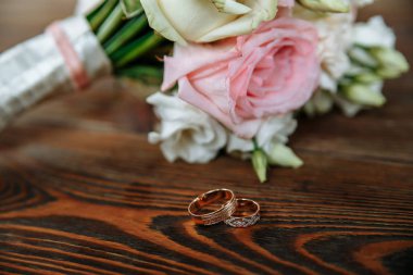 Krem ve pembe gül buketi düğün bir ahşap yüzeye yatıyor. Alyans