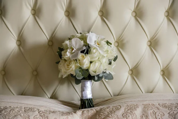 A wedding bouquet of white roses and white orchids stands at the head of the bed. Close up