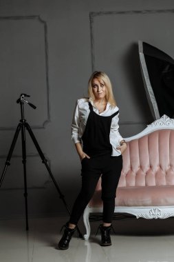 Beyaz gömlekli ve siyah tulumlu güzel bir kız. Pembe bir kanepede. Moda fotoğrafçılığı üzerine bir fotoğraf çekiminde.