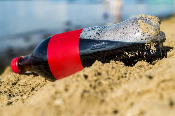Una botella de cola en la arena en la orilla del mar . —  Fotos de Stock