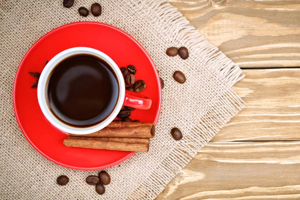 Red ceramic cup with coffee stand on wooden boards and burlap with scattered coffee beans. — Stock Photo, Image
