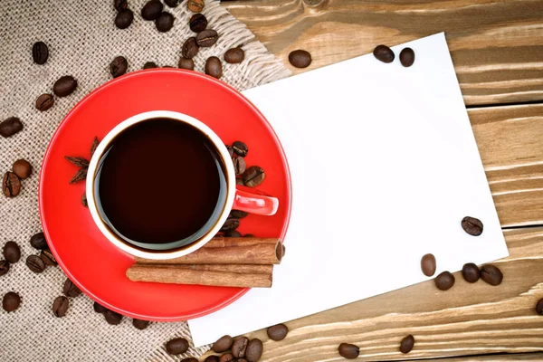 Red ceramic cup with coffee stand on wooden boards and burlap with scattered coffee beans. — Stock Photo, Image